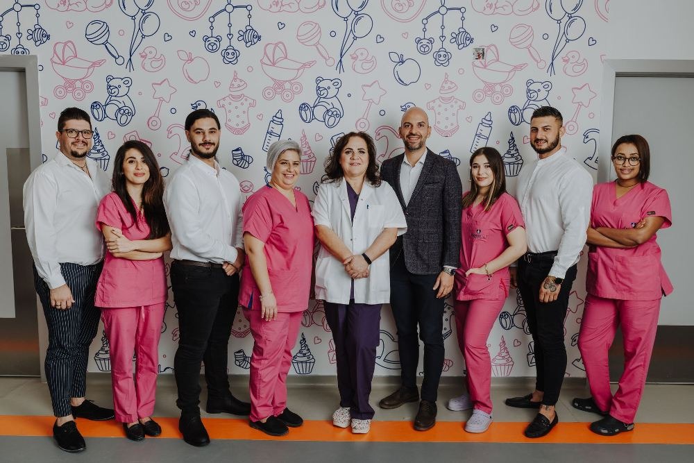 Équipe médicale et paramédicale du Cyprus IVF Hospital, composée de spécialistes en fertilité, debout devant un mur décoré de motifs pour enfants, réunie pour offrir des traitements de PMA aux patients.